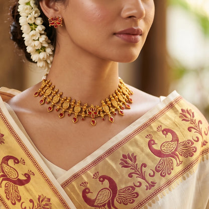 Model wearing a Traditional South Indian matte antique gold temple choker necklace with symmetrical red kemp stones, matching lotus earrings, and an adjustable thread dori