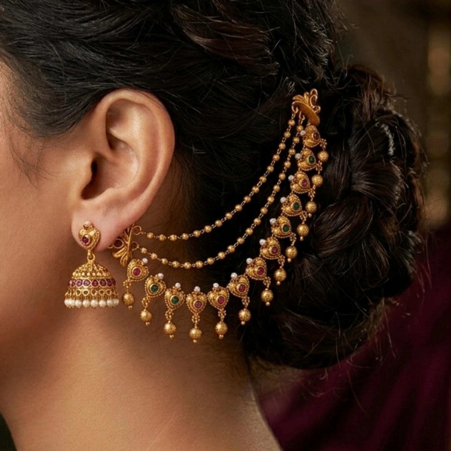 A pair of traditional Indian 3-layer antique gold mattal ear chains with ruby red and emerald green kemp stones, displayed beautifully