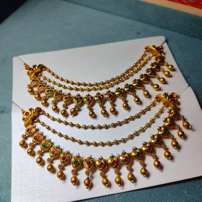 A pair of traditional Indian 3-layer antique gold mattal ear chains with ruby red and emerald green kemp stones, displayed beautifully