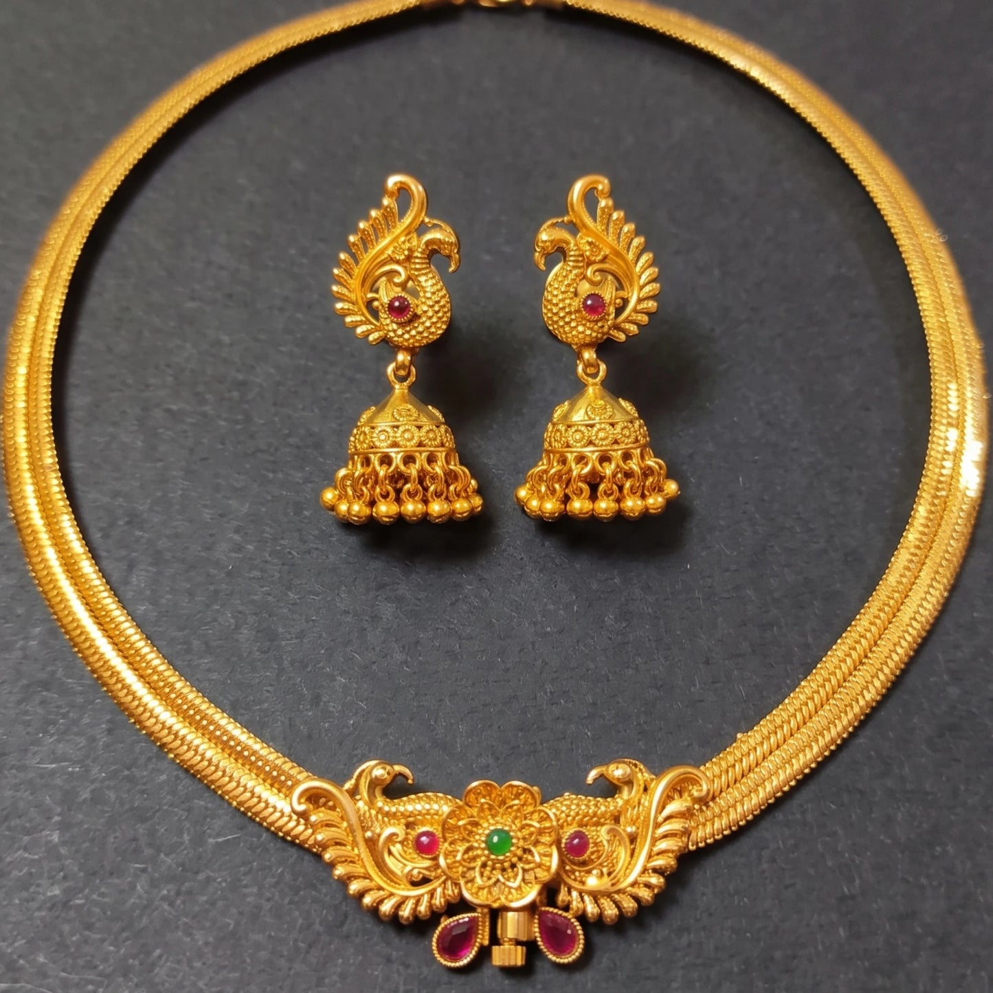 Traditional Indian temple jewelry set featuring a rigid gold peacock collar necklace and dangling Jhumkas in antique gold finish
