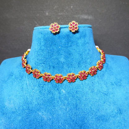 Antique Gold finish jewelry set with red gemstone floral motifs, including a necklace and matching stud earrings, displayed on a blue velvet jewelry bust against a dark gray background.