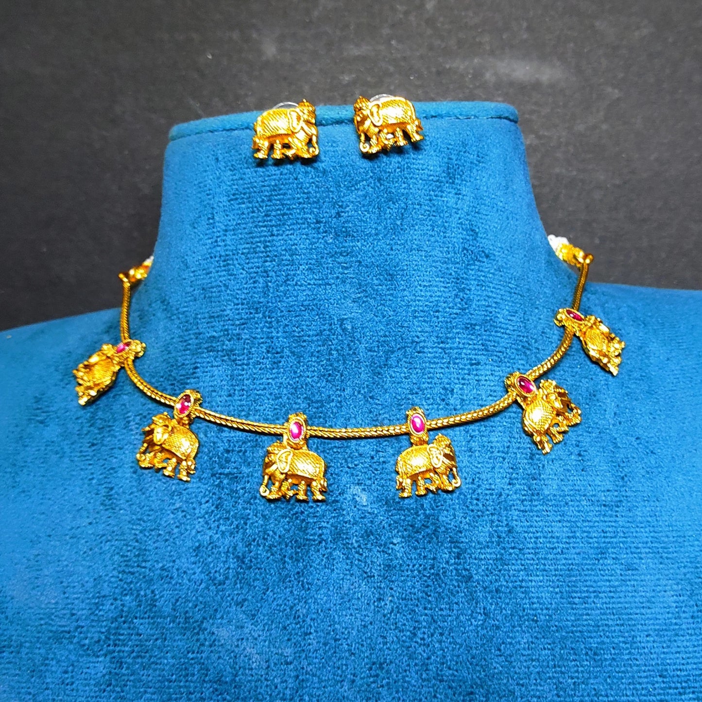 Gold-toned jewelry set displayed on a blue velvet jewelry bust, featuring an elephant-themed necklace with matching stud earrings.