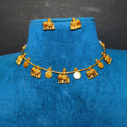 A gold-toned jewelry set displayed on a blue velvet bust, featuring a necklace with small elephant and coin-shaped charms and matching stud earrings.