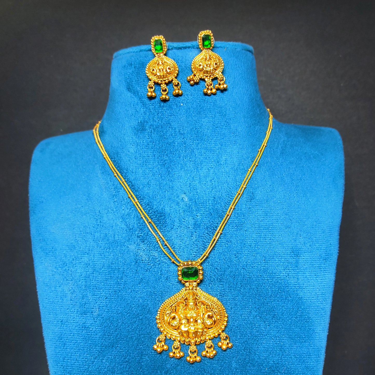 Antique Gold Finish necklace and earrings with green gemstones on a blue mannequin bust against a dark background