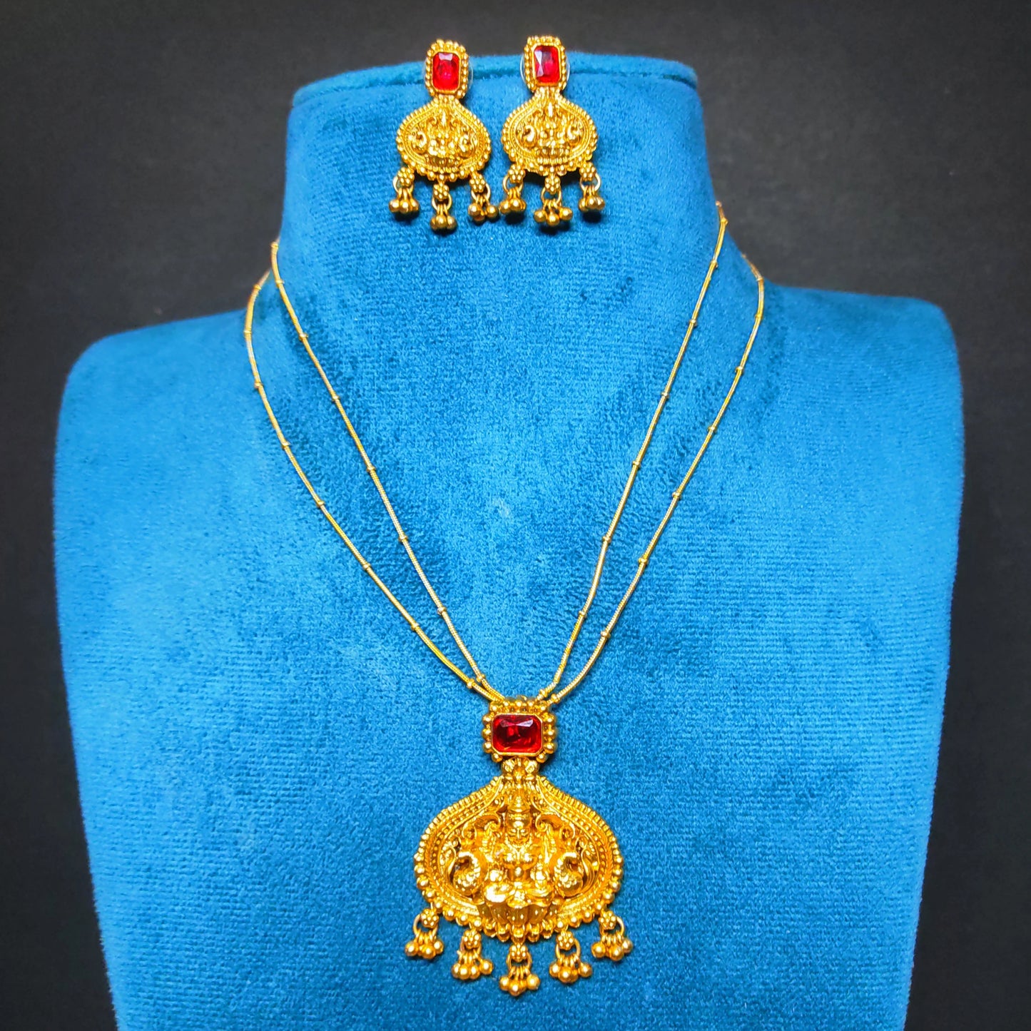 Antique Gold finish necklace and earrings set on a blue velvet stand against a black background