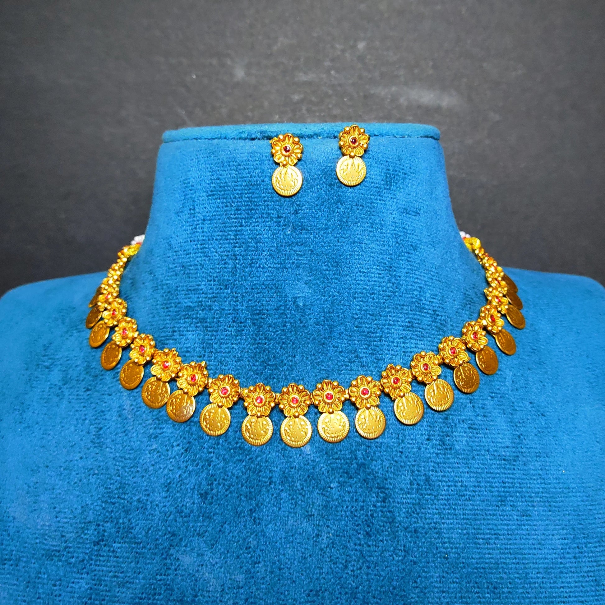 Antique gold finish coin necklace and matching stud earrings displayed on a blue velvet jewelry bust against a dark gray background.