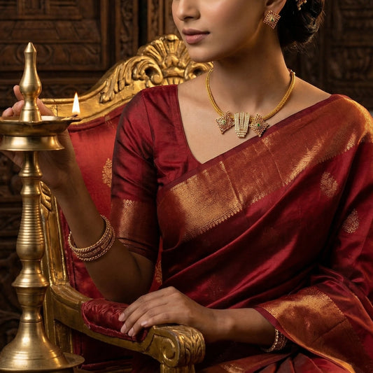 Woman in traditional maroon saree with gold toned religious jewelry holding a brass lamp.
