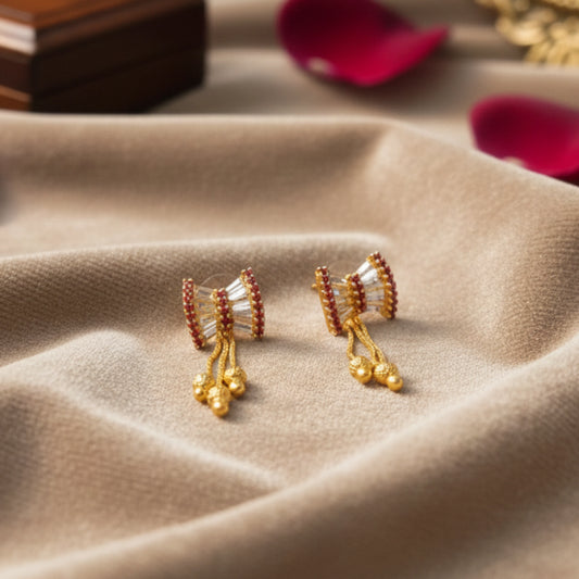 Gold plated earrings with red accents on a beige fabric surface