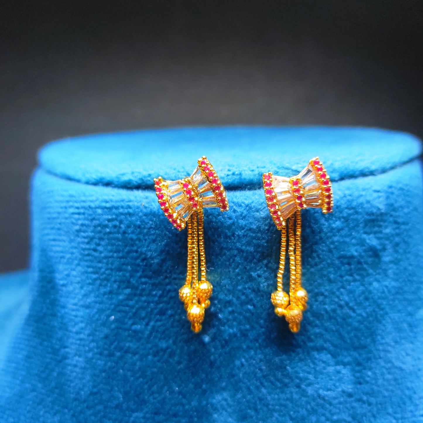 Gold plated and red beaded earrings on a blue cushion