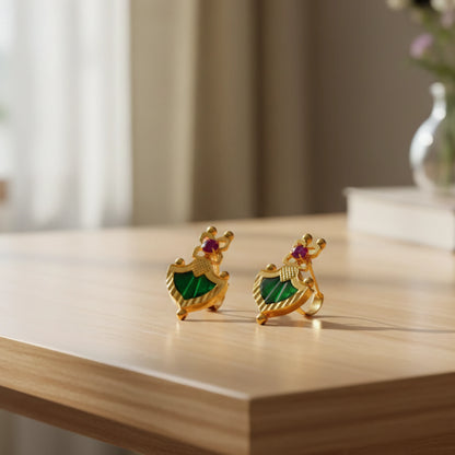 Gold plated earrings with green palakka and ruby red stones on a wooden surface