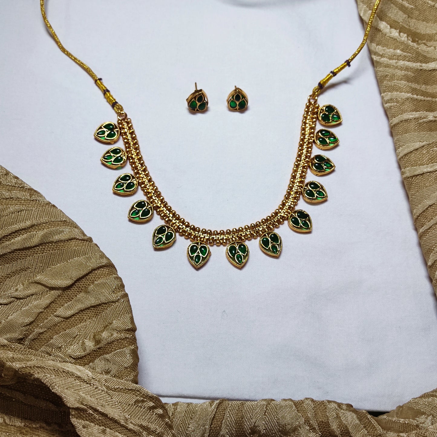 Gold toned necklace with green gemstones and matching earrings on a white and gold fabric background