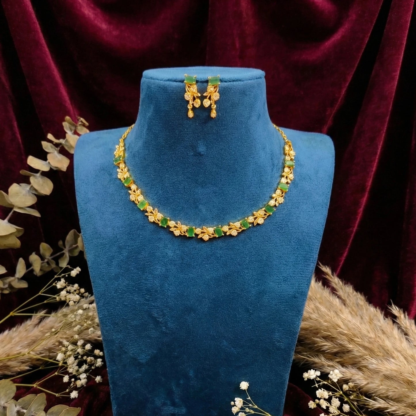 Gold plated necklace and earrings on a blue mannequin bust with a red curtain background