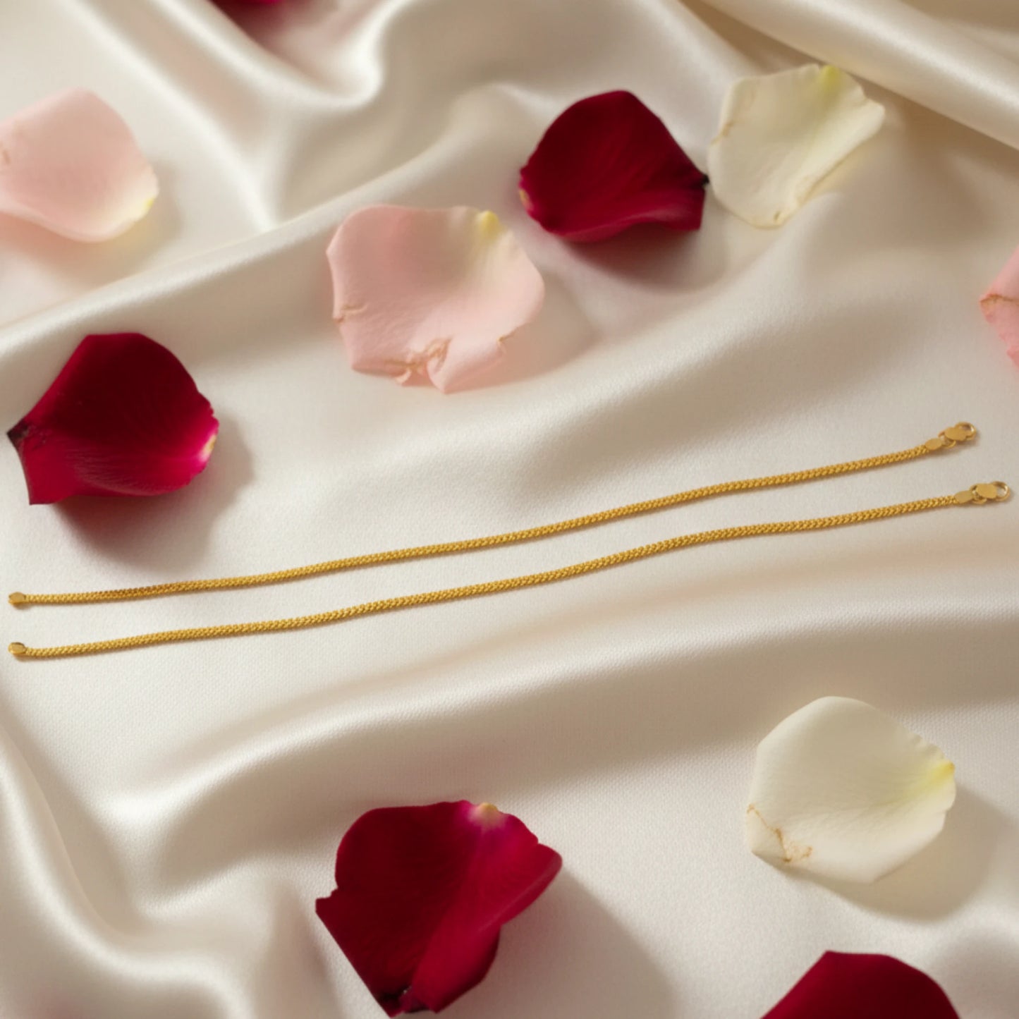 Gold plated Anklet Pair jewelry on a white fabric background with scattered rose petals
