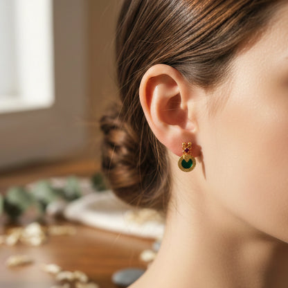 Close-up of a woman wearing a gold plated earring with a green palakka and ruby red gemstone, blurred background