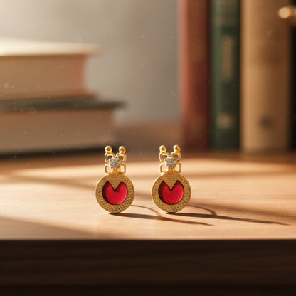 Gold plated earrings with red palakka and white stone design on a wooden surface