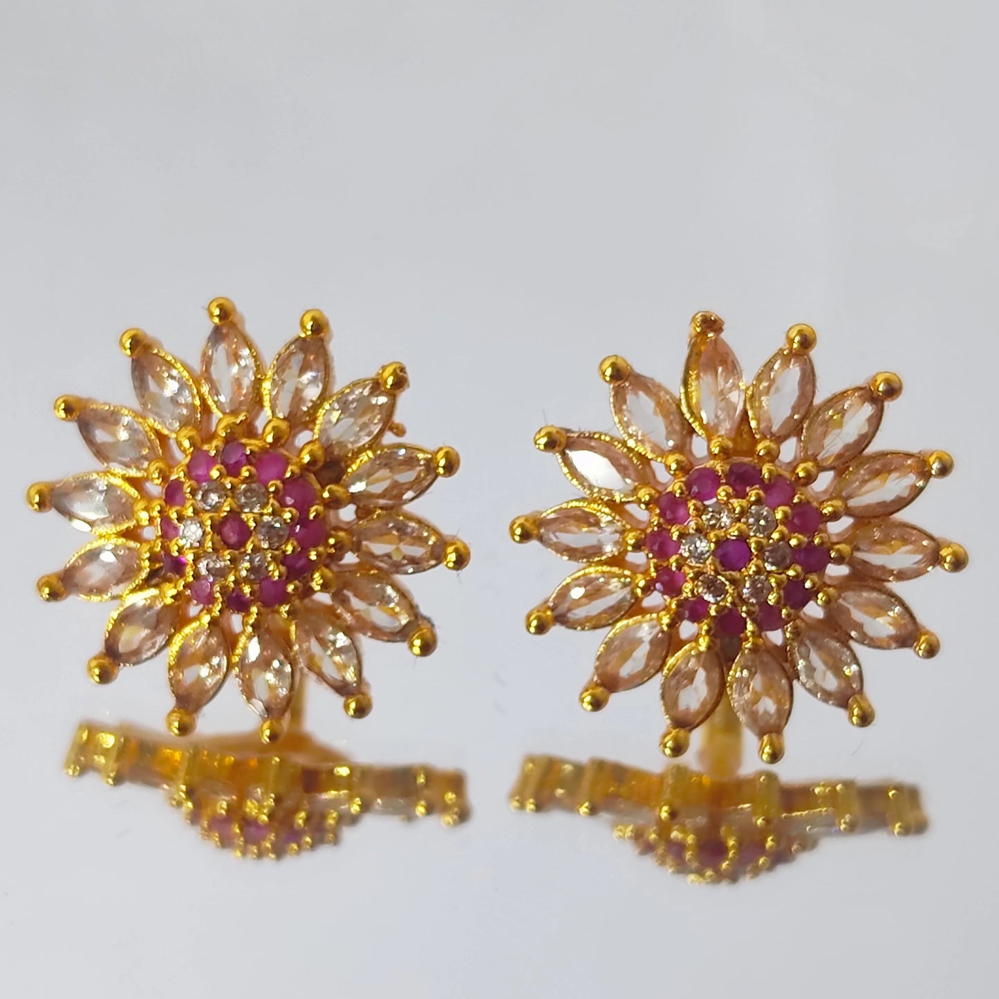 Gold plated earrings in floral stud form with multicolor AD stones displayed on a reflective surface