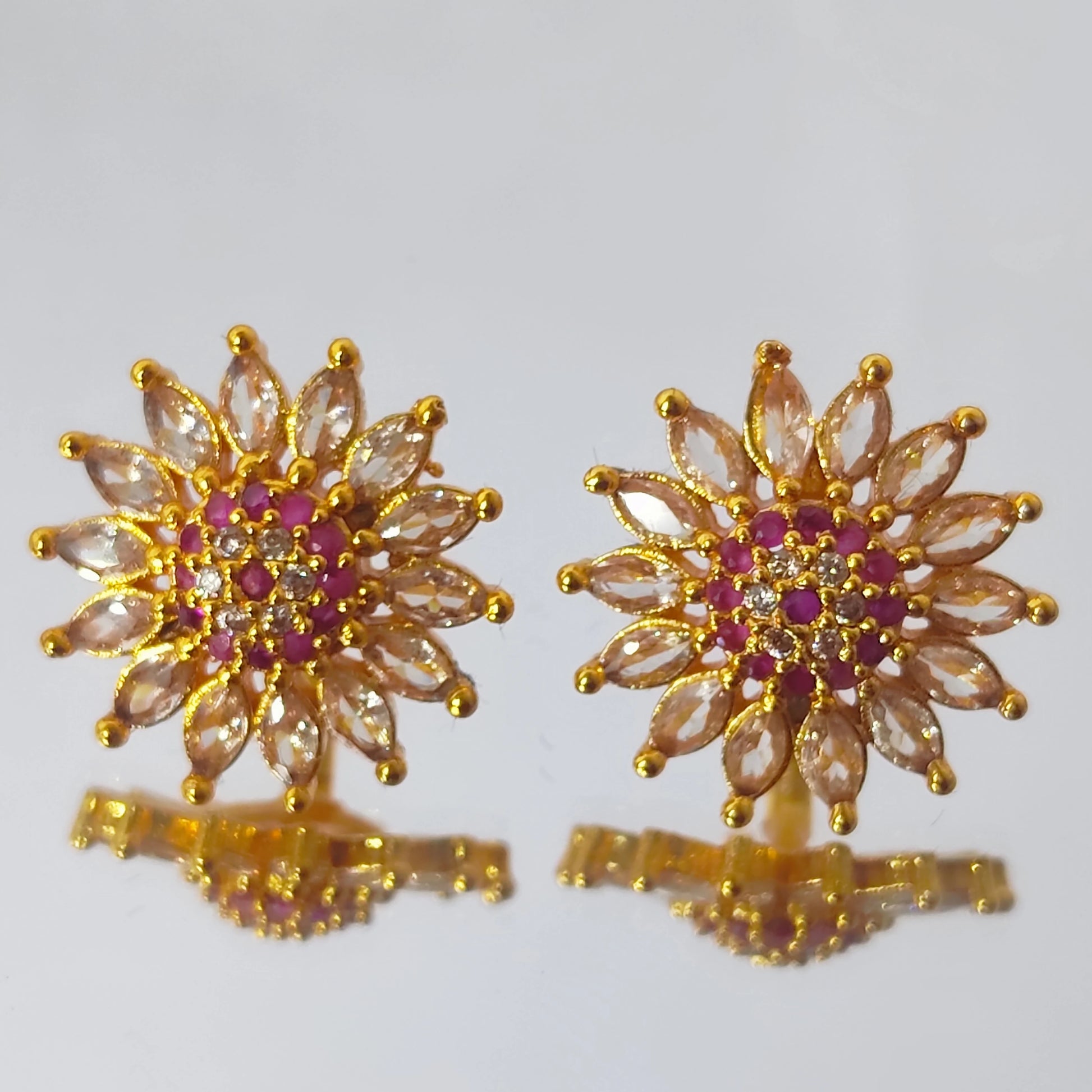 Gold plated earrings in floral stud form with multicolor AD stones displayed on a reflective surface