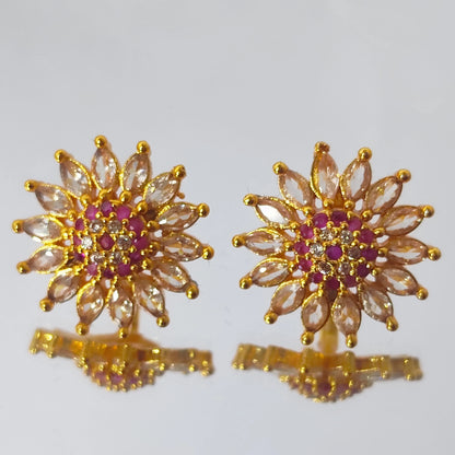 Gold plated earrings in floral stud form with multicolor AD stones displayed on a reflective surface