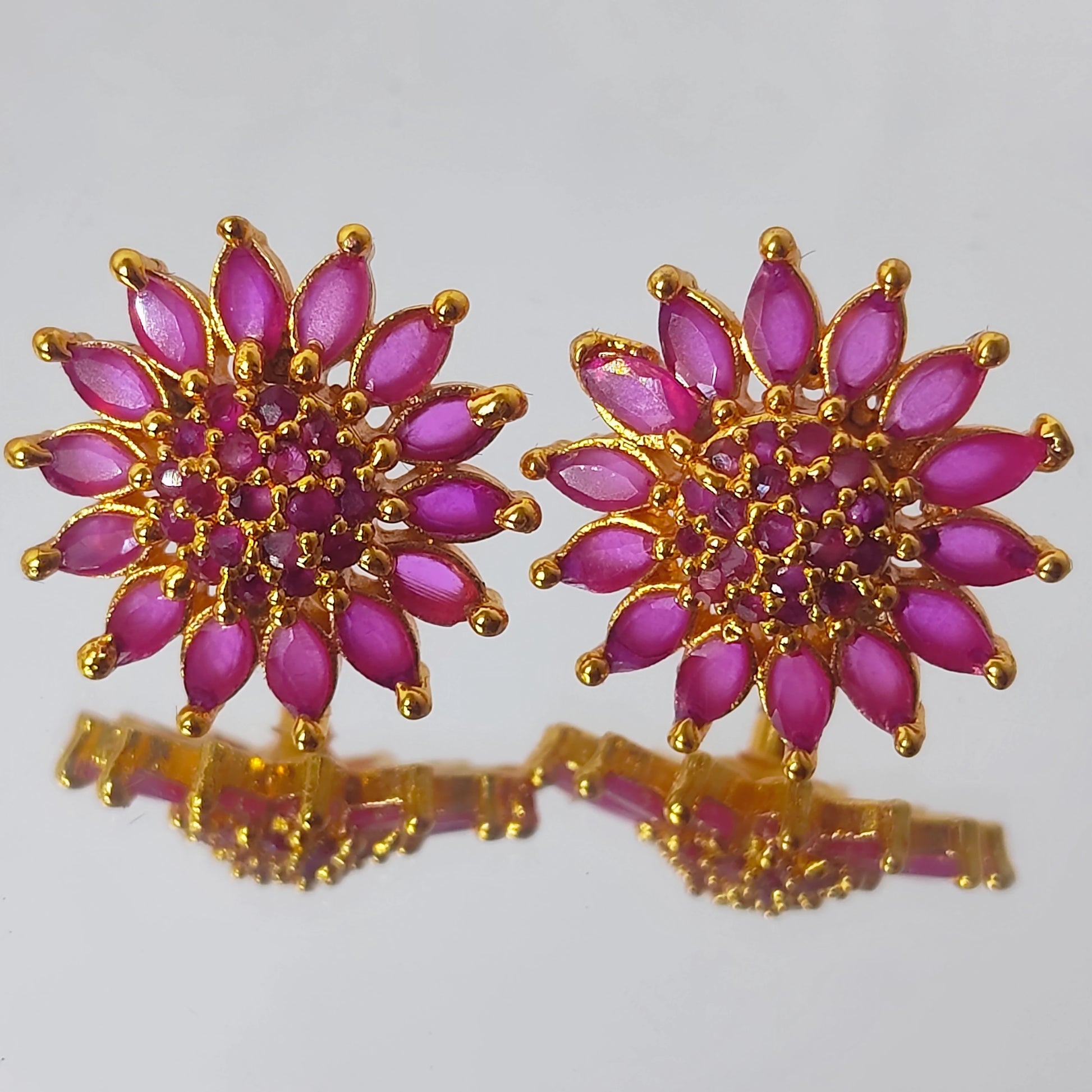 Pair of gold plated AD floral sunburst stud earrings on a reflective surface.