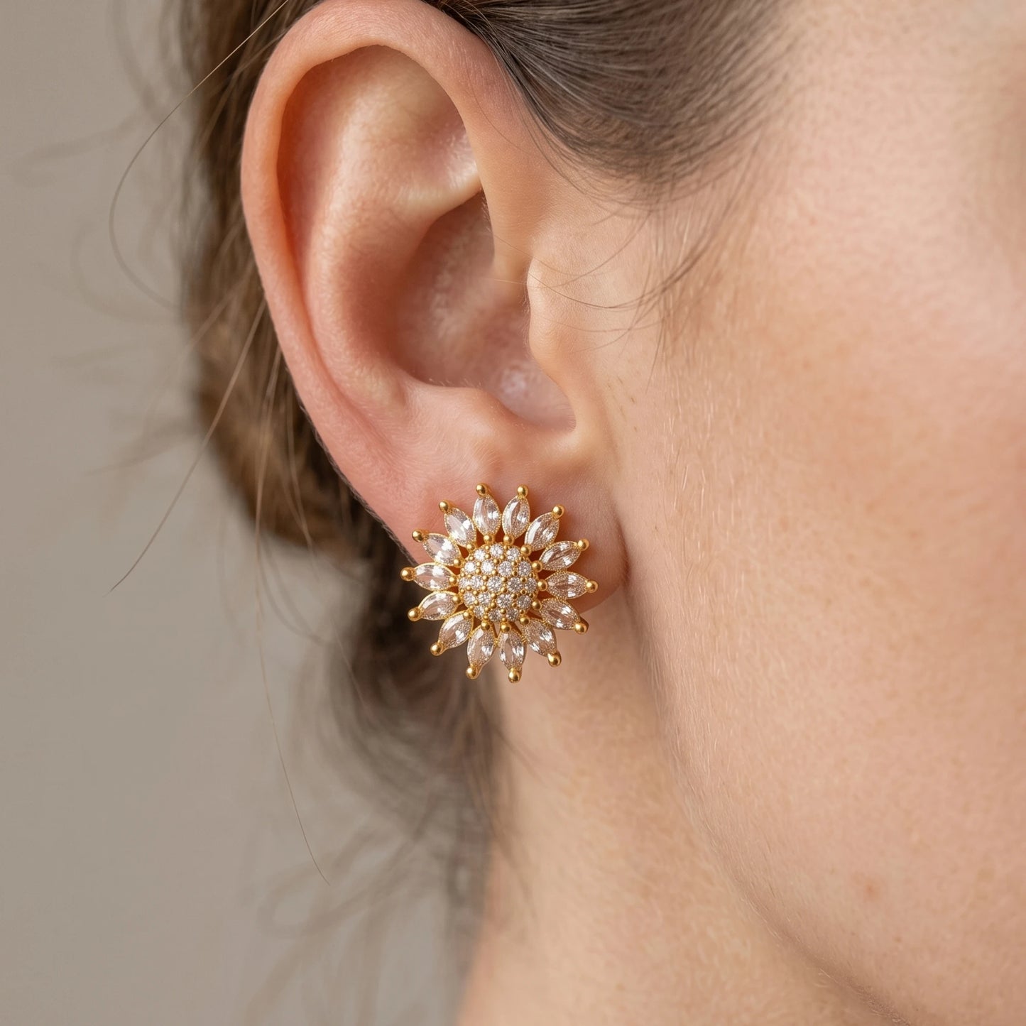 Close-up of an ear wearing a gold plated AD floral sunburst earring against a neutral background