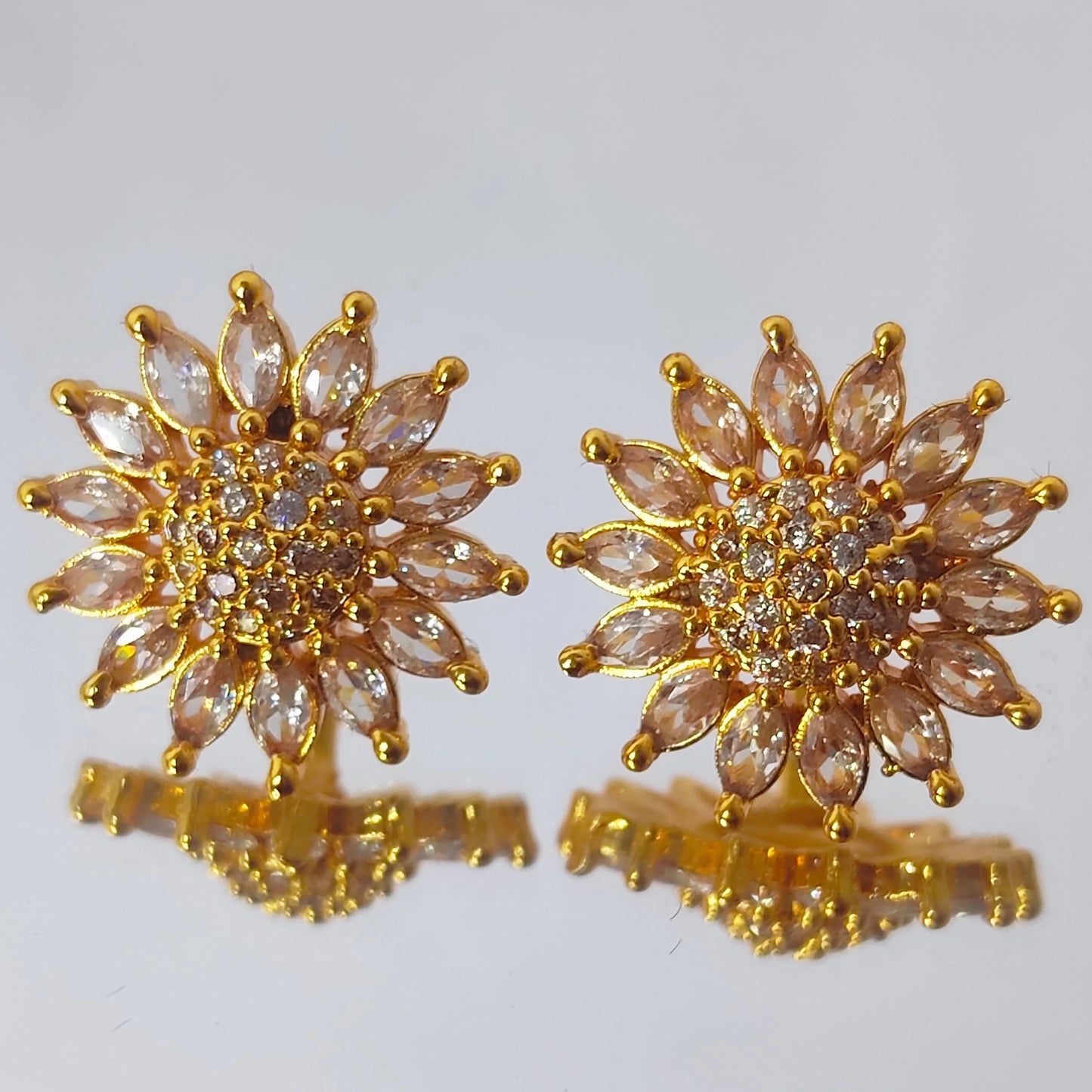 Gold plated AD floral sun burst stud earrings with clear stones on a white background