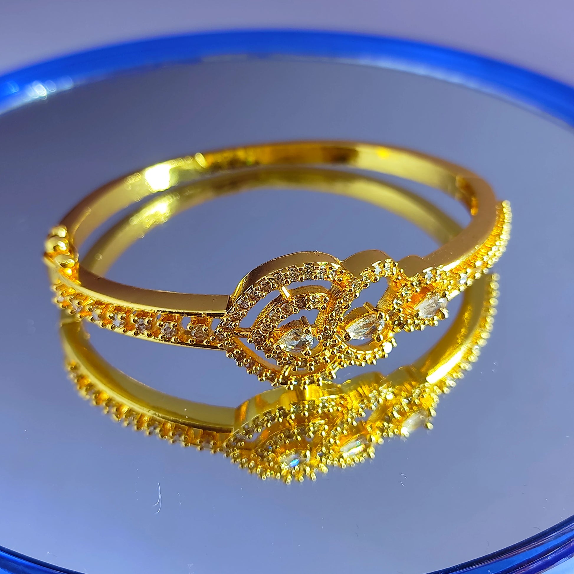 Gold plated bracelet with intricate design on a reflective blue surface