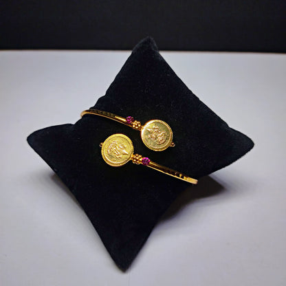 Gold plated bracelet with coin designs on a black pillow against a white background