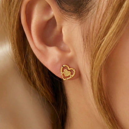 Gold plated heart-shaped earring worn by a person with blonde hair.