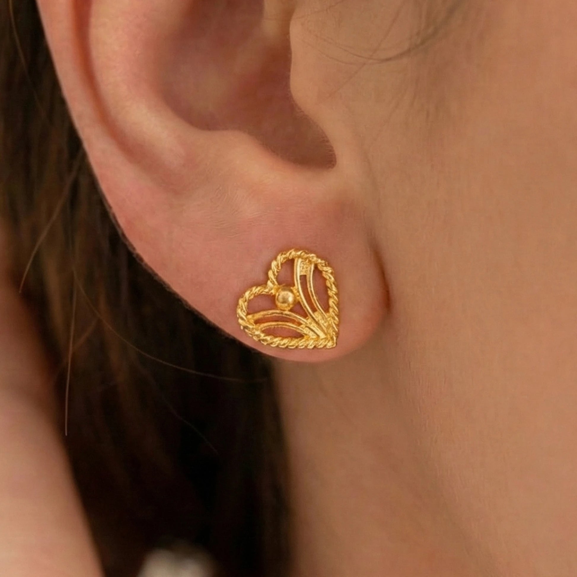 Gold plated heart-shaped earring worn on an ear with a blurred background
