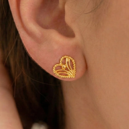 Gold plated heart-shaped earring worn on an ear with a blurred background
