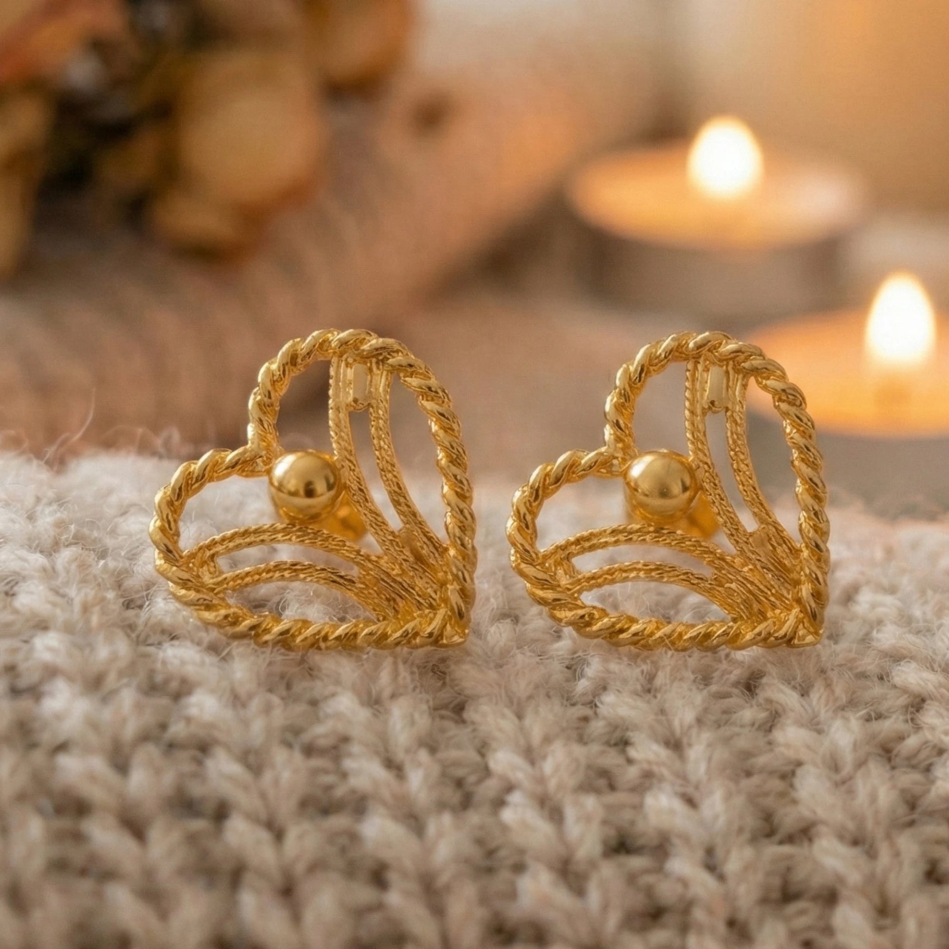 Gold plated earrings on a textured surface with a warm, blurred background