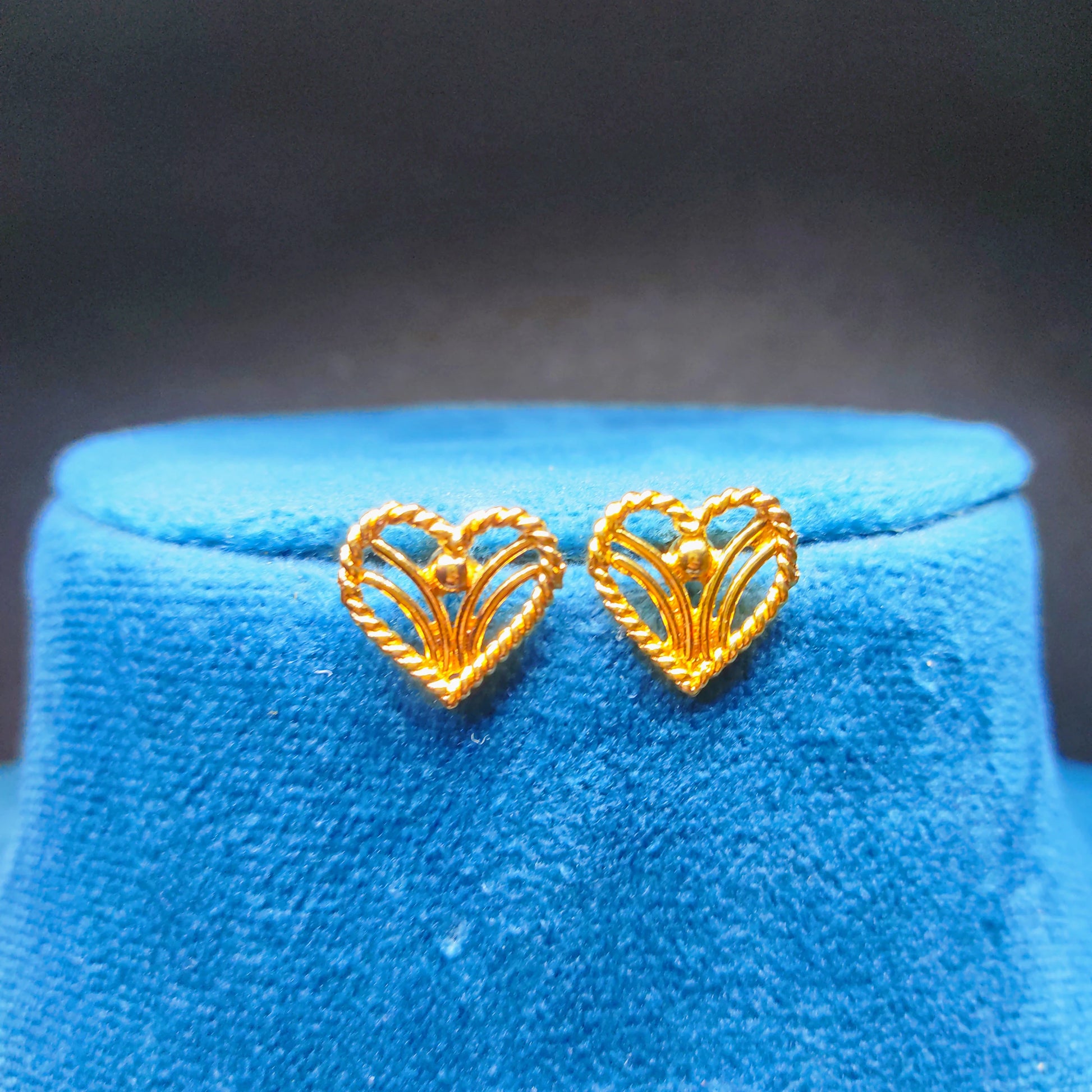 Gold plated heart-shaped earrings on a blue cushion with a dark background