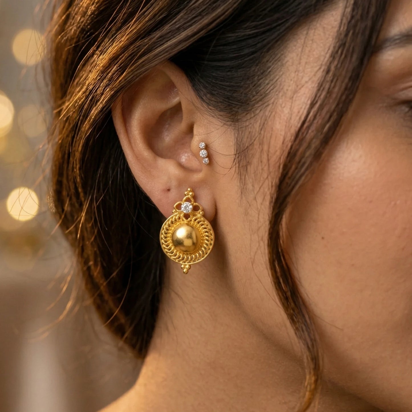 Close-up of a woman's ear wearing gold plated earrings with a blurred background