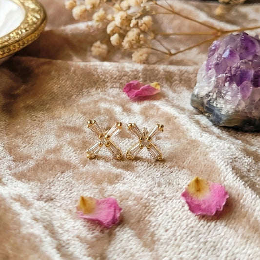 Gold plated 'XX' earrings on a textured surface with flowers and crystals