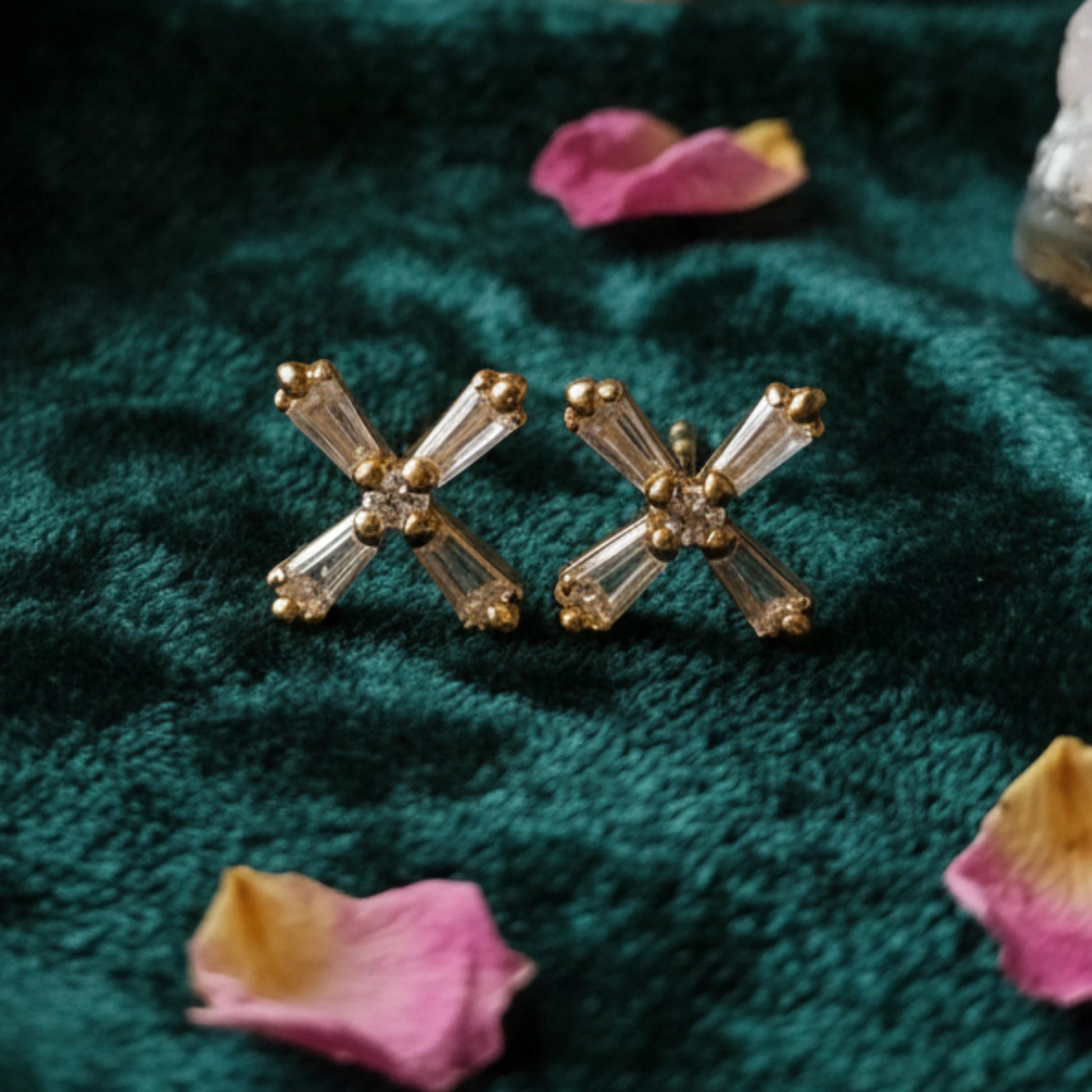 Gold plated crystal stud earrings on a textured green surface with pink petals.