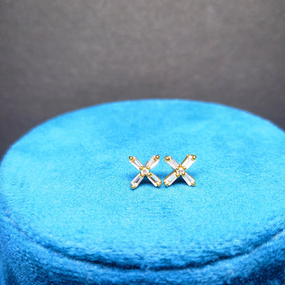 Gold plated 'X' shaped earrings on a blue cushion with a gray background