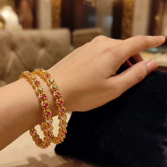 Gold plated bangles with pink stones on a hand against a blurred indoor background
