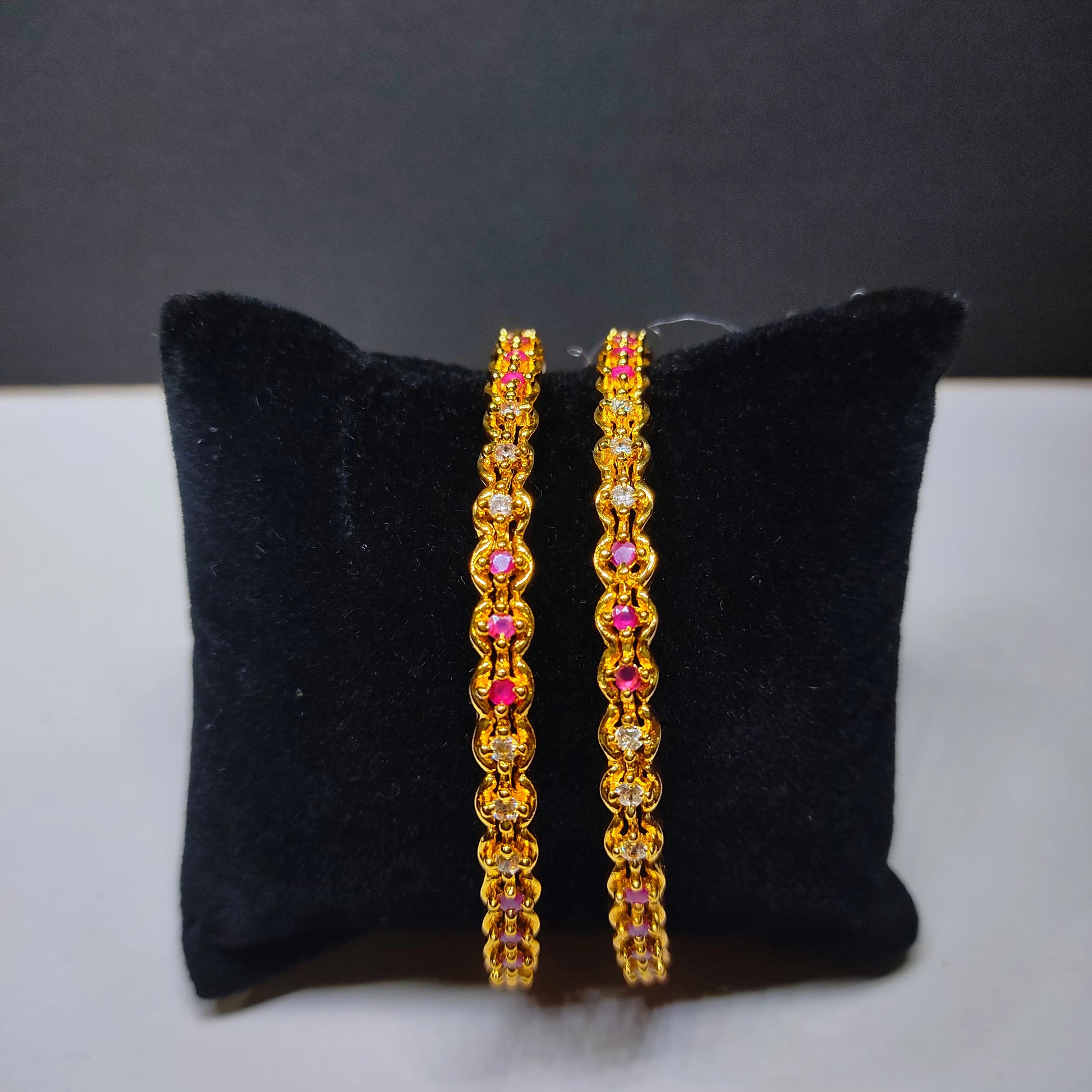 Gold plated pink and white stones  beaded bangles on a black cushion with a gray background