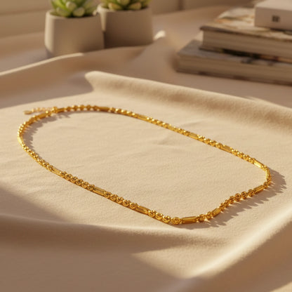 Gold plated neckchain with beaded and cylindrical pattern on a beige surface with a soft focus background