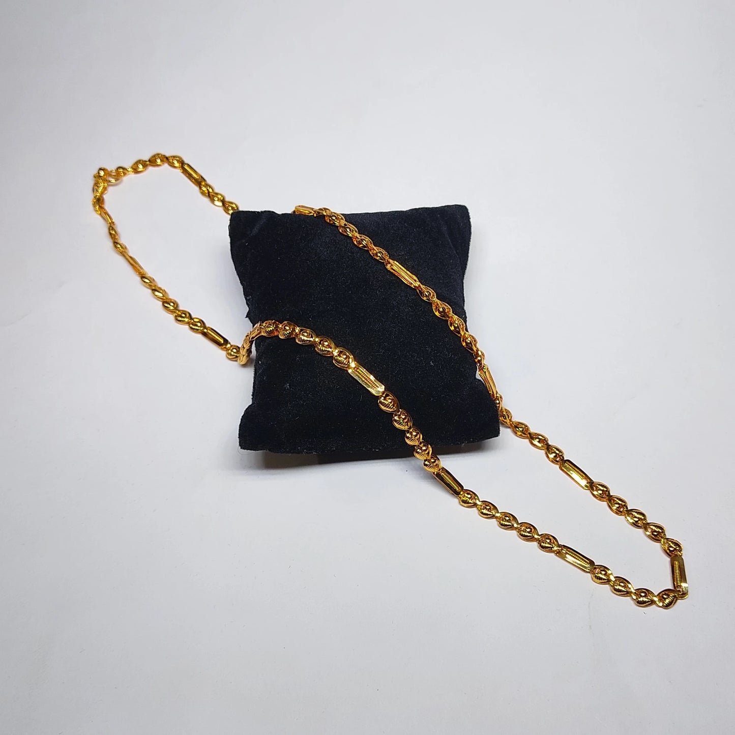  gold plated neckchain with beads and cylindrical pattern on a black cushion
