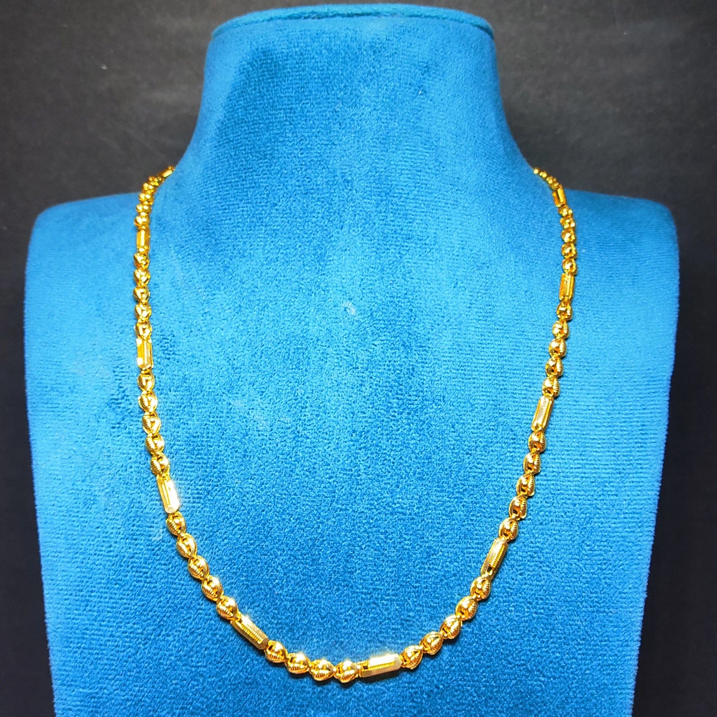 Gold plated neckchain with beeads and cylindrical pattern on a beige surface with a soft focus background
