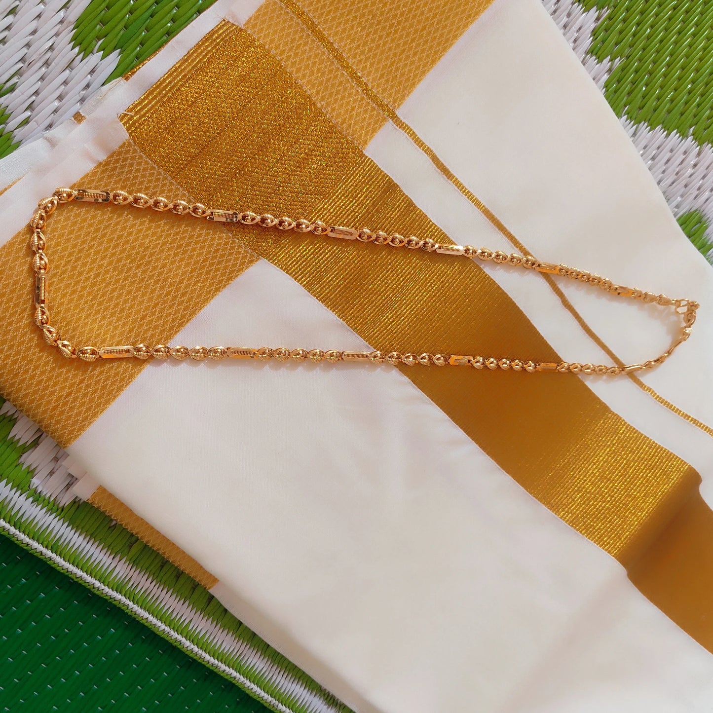 Gold plated neck chain with beads and cylindrical pattern on a fabric background with green and white pattern