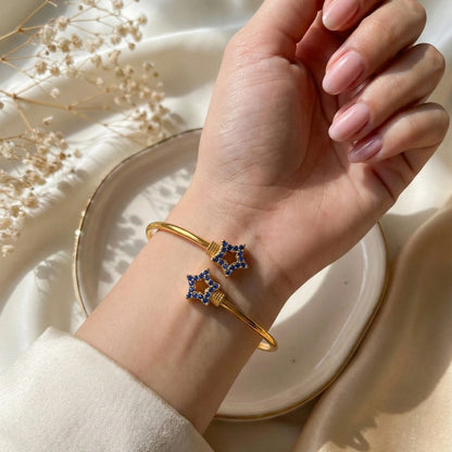 Gold plated bracelet with blue stones on a hand against a neutral background