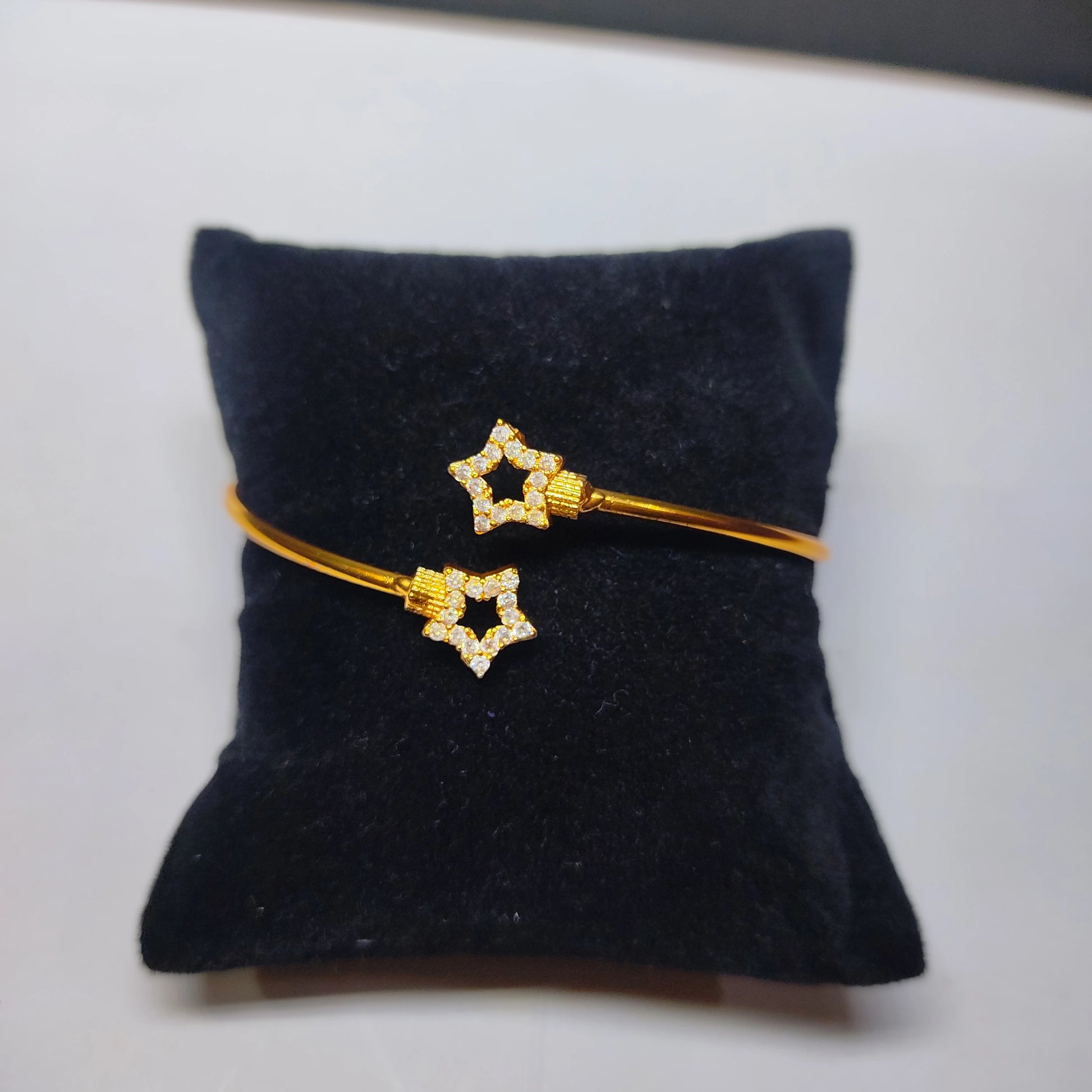 Gold plated bracelet with star-shaped ends on a black cushion