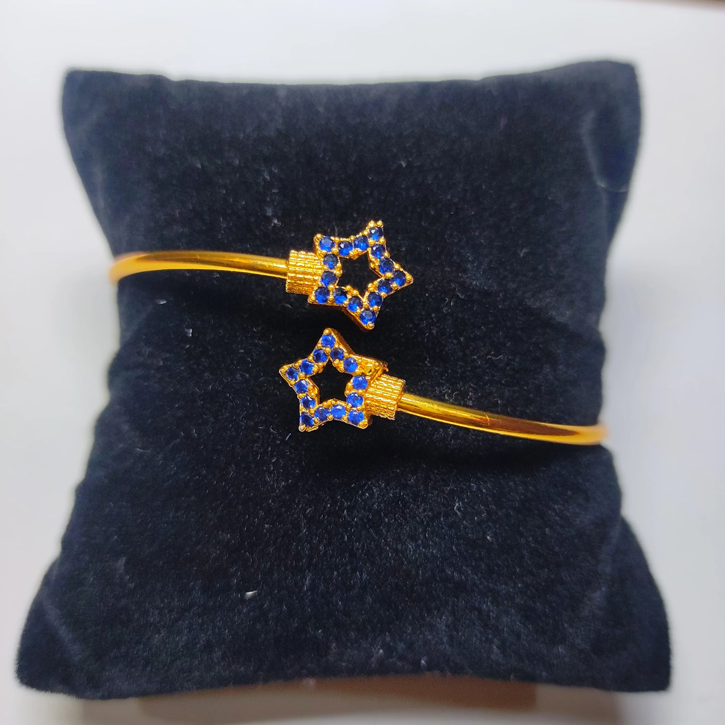 Gold plated bracelets with star-shaped blue gemstones on a dark blue cushion