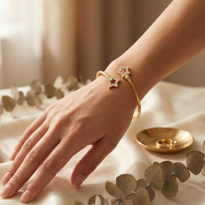 Hand wearing a gold plated bracelet with star design on a neutral background