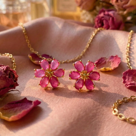 Pink flower-shaped earrings with gold accents on a pink fabric background with dried roses.