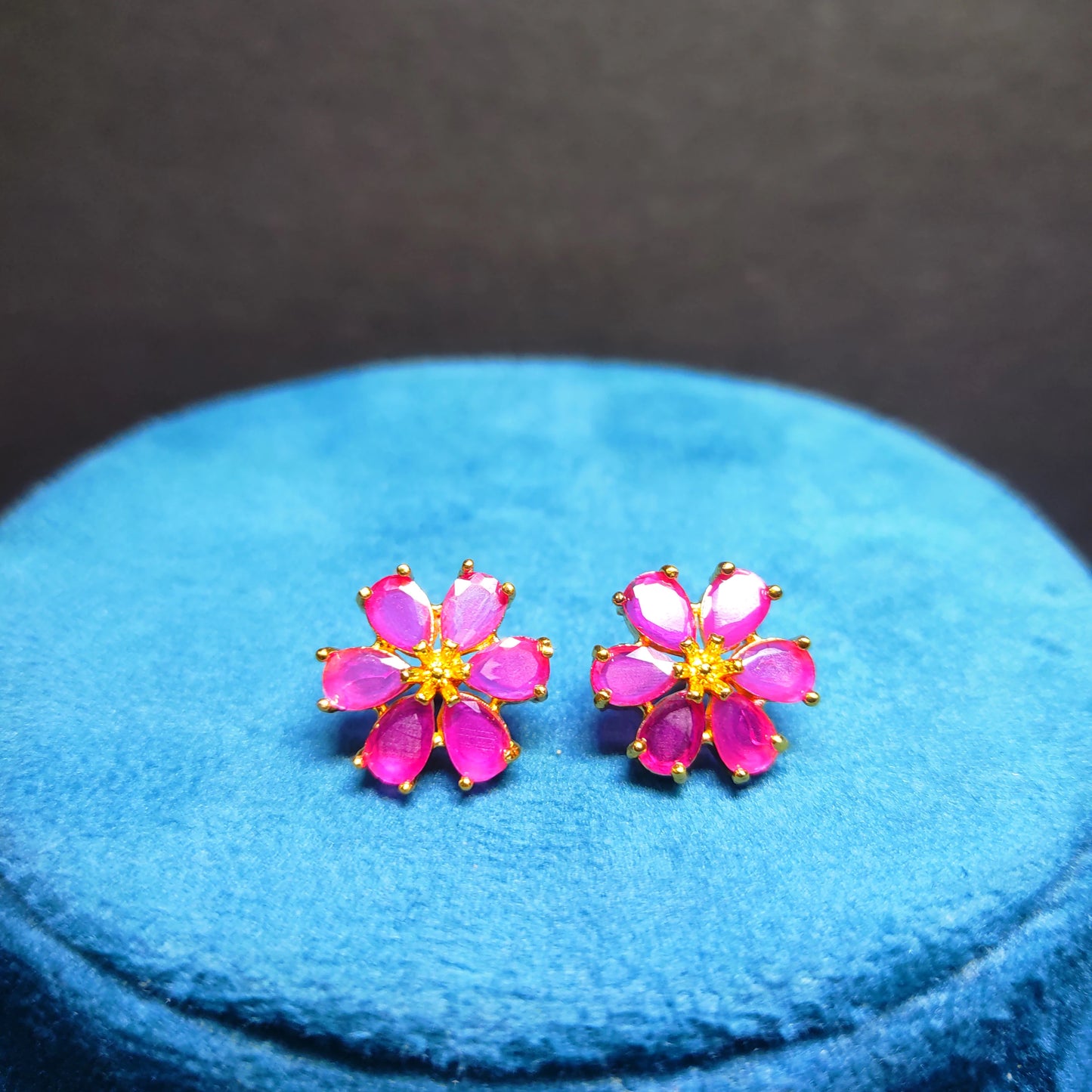 Gold Plated Pink flower-shaped earrings on a blue cushion with a dark background