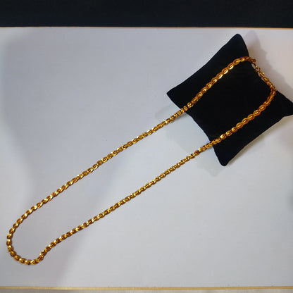 Gold plated chain on a black pillow against a white background