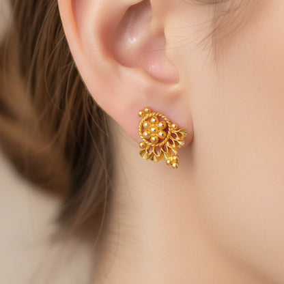 Gold plated earring worn on an ear with a blurred background